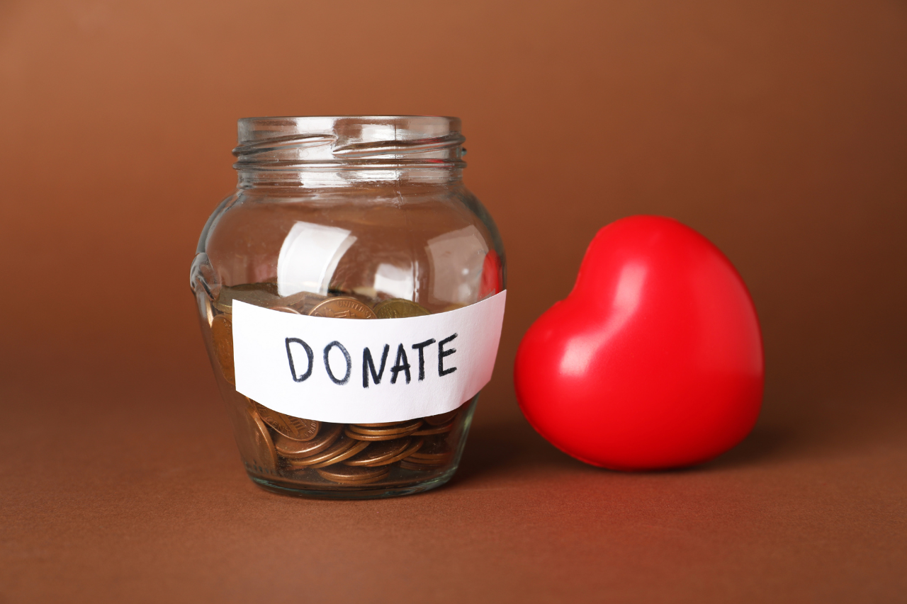 Jam jar of coins with a label on to say donate. The jar sits next to a red heart